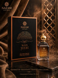 Nazam Perfumes Black Suede 25ml premium Arabic attar bottle with a gold dome cap next to its black and gold presentation box on a reflective marble table.
