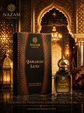 Nazam Perfumes Qamarah Luxe 25ml premium Arabic attar bottle with a gold dome cap next to its deep brown presentation box on a reflective table.