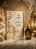 Nazam Perfumes Silken Oud 25ml premium Arabic attar bottle with a gold dome cap next to its cream and gold geometric presentation box on a reflective marble table.